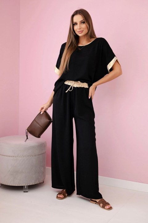 Modelka w czarnym komplecie z wiskozy ze złotym obszyciem – elegancki włoski zestaw z szerokimi spodniami i luźną bluzką Modelka w czarnym komplecie z wiskozy ze złotym obszyciem – elegancki włoski zestaw z szerokimi spodniami i luźną bluzką