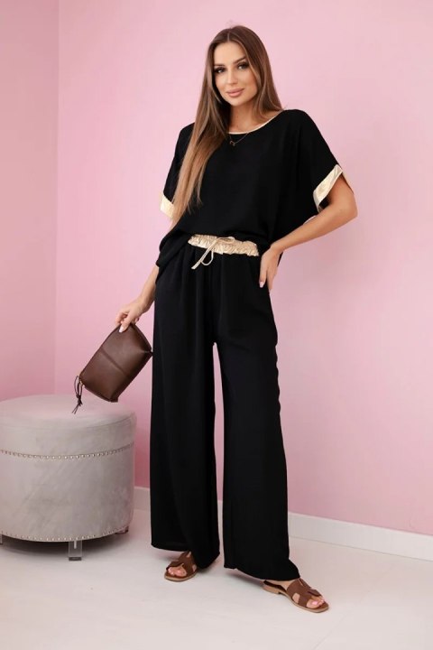 Modelka w czarnym komplecie z wiskozy ze złotym obszyciem – elegancki włoski zestaw z szerokimi spodniami i luźną bluzką Modelka w czarnym komplecie z wiskozy ze złotym obszyciem – elegancki włoski zestaw z szerokimi spodniami i luźną bluzką