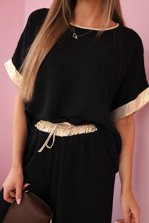 Modelka w czarnym komplecie z wiskozy ze złotym obszyciem – elegancki włoski zestaw z szerokimi spodniami i luźną bluzką Modelka w czarnym komplecie z wiskozy ze złotym obszyciem – elegancki włoski zestaw z szerokimi spodniami i luźną bluzką
