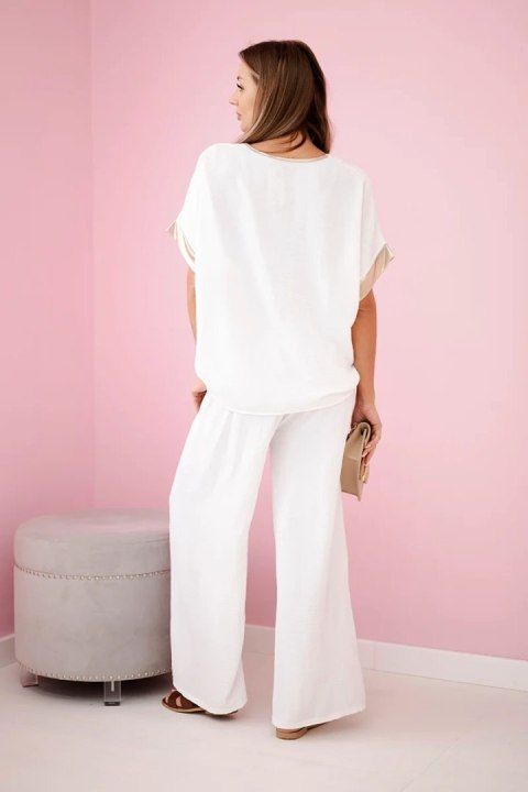 Modelka w ecru komplecie z wiskozy ze złotym obszyciem – elegancki zestaw z szerokimi spodniami i luźną bluzką Modelka w ecru komplecie z wiskozy ze złotym obszyciem – elegancki zestaw z szerokimi spodniami i luźną bluzką