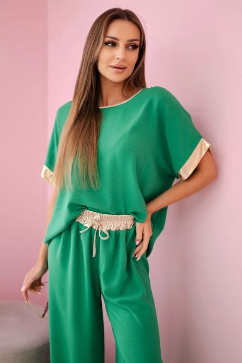 Modelka w zielonym komplecie z wiskozy ze złotym obszyciem – stylowy włoski zestaw z szerokimi spodniami i luźną bluzką Modelka w zielonym komplecie z wiskozy ze złotym obszyciem – stylowy włoski zestaw z szerokimi spodniami i luźną bluzką