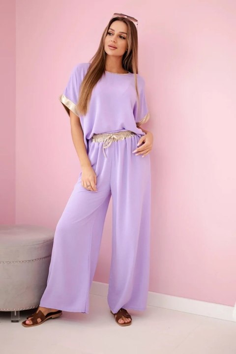 Modelka w jasnofioletowym komplecie z wiskozy ze złotym obszyciem – elegancki włoski zestaw z luźną bluzką i szerokimi spodniami Modelka w jasnofioletowym komplecie z wiskozy ze złotym obszyciem – elegancki włoski zestaw z luźną bluzką i szerokimi spodniami