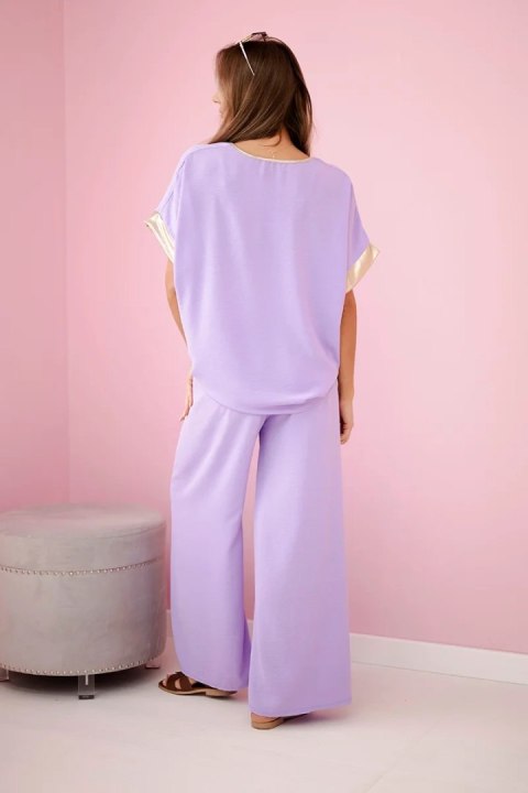 Modelka w jasnofioletowym komplecie z wiskozy ze złotym obszyciem – elegancki włoski zestaw z luźną bluzką i szerokimi spodniami Modelka w jasnofioletowym komplecie z wiskozy ze złotym obszyciem – elegancki włoski zestaw z luźną bluzką i szerokimi spodniami