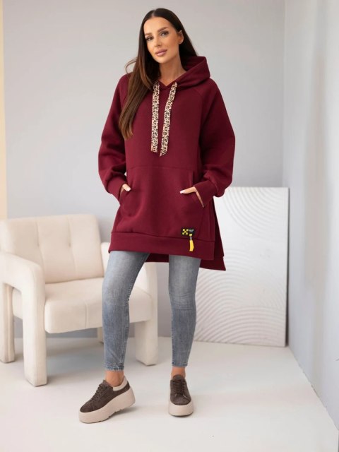 Modelka w bordowej bluzie oversize z kapturem, sznurkiem w panterkę i kieszenią kangurką oraz szarych jeansach