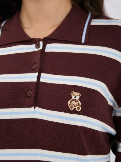 Zbliżenie na kołnierzyk, trzy guziki i haftowanego misia na brązowym swetrze polo w paski ITALY MODA.