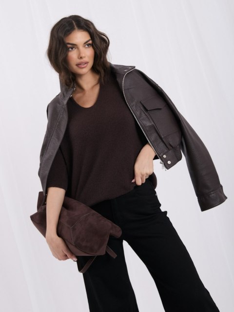 Modelka w czekoladowym swetrze ITALY MODA, brązowej kurtce i czarnych spodniach, z torebką pod pachą.